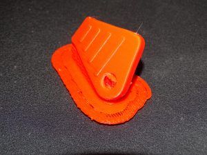 Une coque de clé orange imprimée en 3D avec ses supports d'impression
