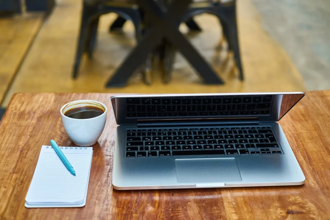 Ordinateur, avec bloc-notes, stylo et café posés sur une table en bois
